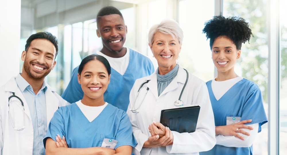 A diverse group of healthcare professionals stands together, wearing scrubs and lab coats, with warm smiles in a bright hospital setting. A diverse group of healthcare professionals stands together, wearing scrubs and lab coats, with warm smiles in a bright hospital setting.