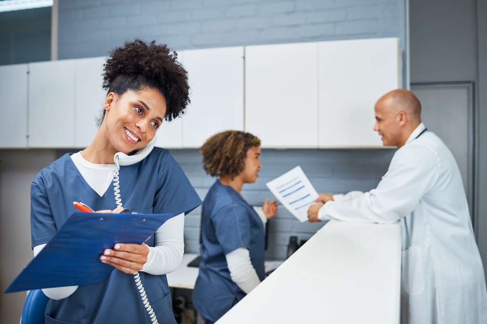 A woman in scrubs is positioned at a counter with two others, participating in a discussion A woman in scrubs is positioned at a counter with two others, participating in a discussion